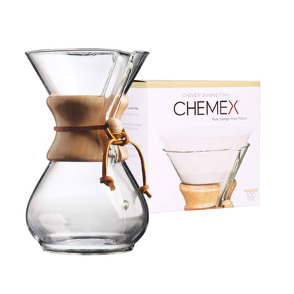 Eine Develop-Koffein-Kaffeemaschine aus Glas mit Holzkragen steht neben ihrer Markenschachtel, die ein Filterbild zeigt.