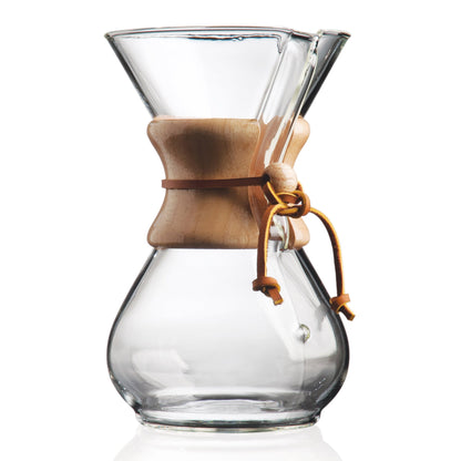 Ein klarer Chemex-Kaffeezubereiter aus Glas mit einem Holzkragen und einem Lederband in der Mitte.